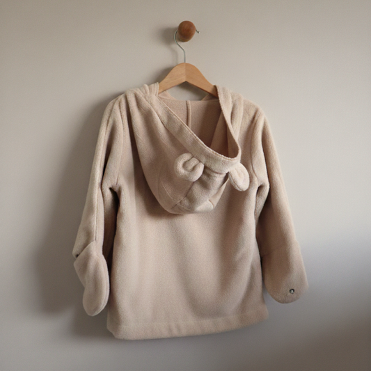 Beige children's jacket with a hood on a wooden hanger against a plain wall.