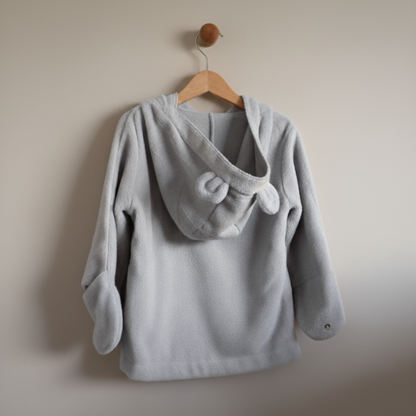 Gray children's sweater with a hood on a wooden hanger against a beige wall.