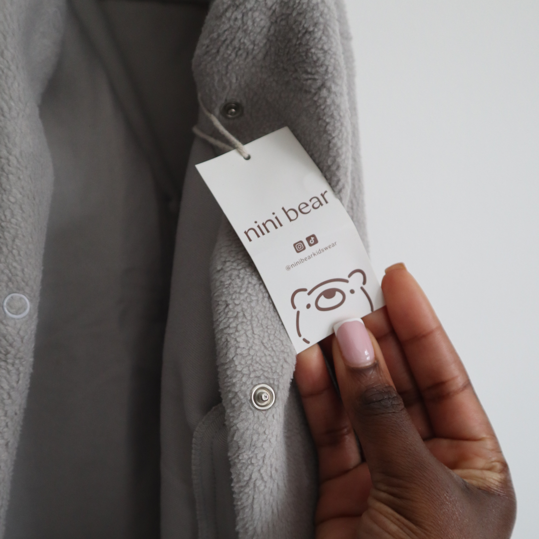 Gray fleece jacket with a 'nini bear' tag held by a hand.